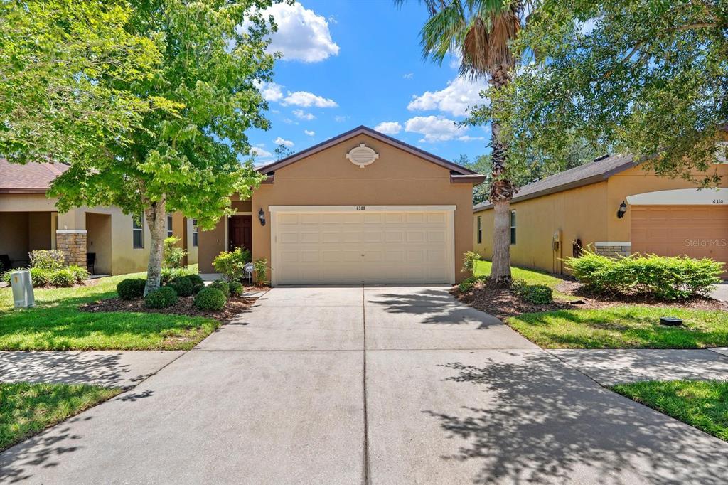 A single-story suburban house with a tan stucco exterior, a two-car garage, and a driveway — 6308 MAGNOLIA PARK BOULEVARD, RIVERVIEW, FL