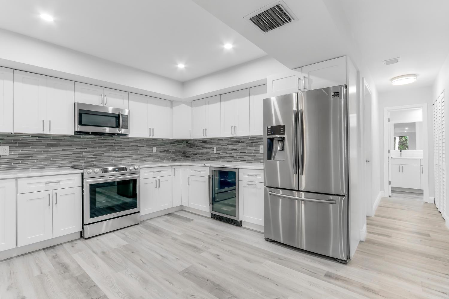 A modern kitchen features white cabinetry, stainless steel appliances, and a gray tiled backsplash — 22874 Ironwedge Drive, Boca Raton FL 33433, BOCA RATON, FL