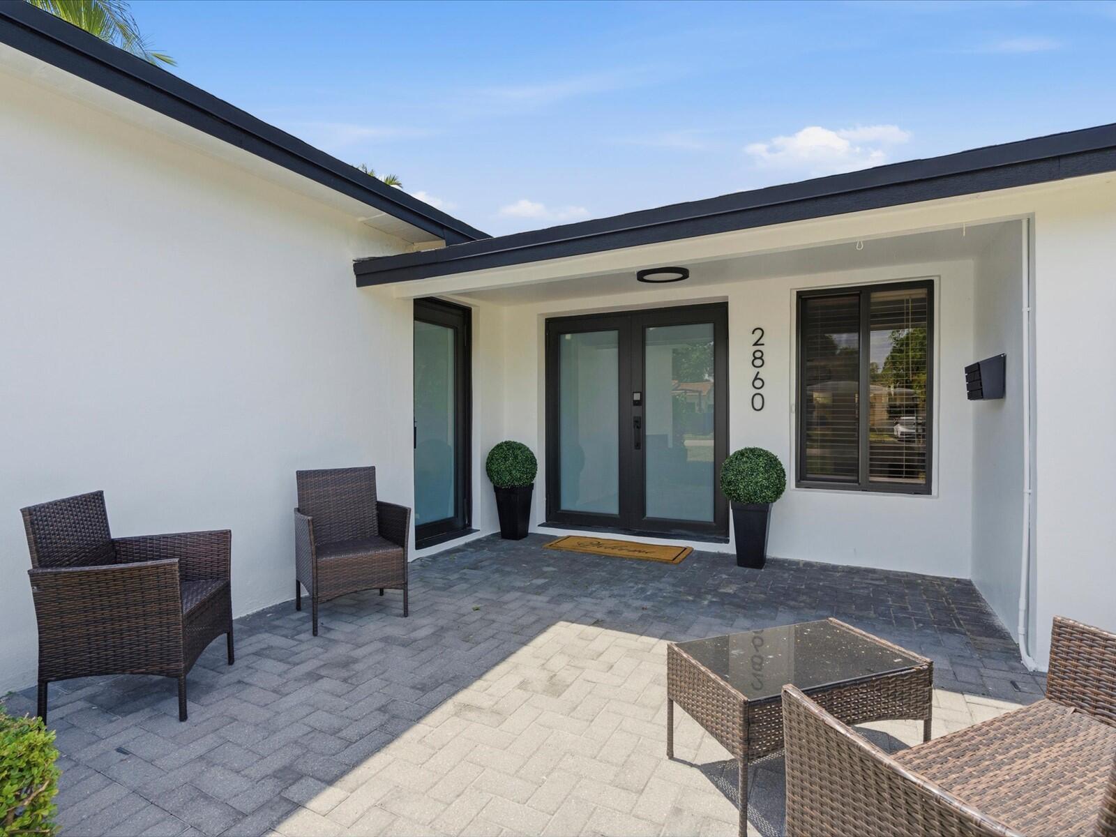 A patio with wicker furniture sits in front of a house with white walls — 2860 Monroe Street, Hollywood FL 33020, HOLLYWOOD, FL