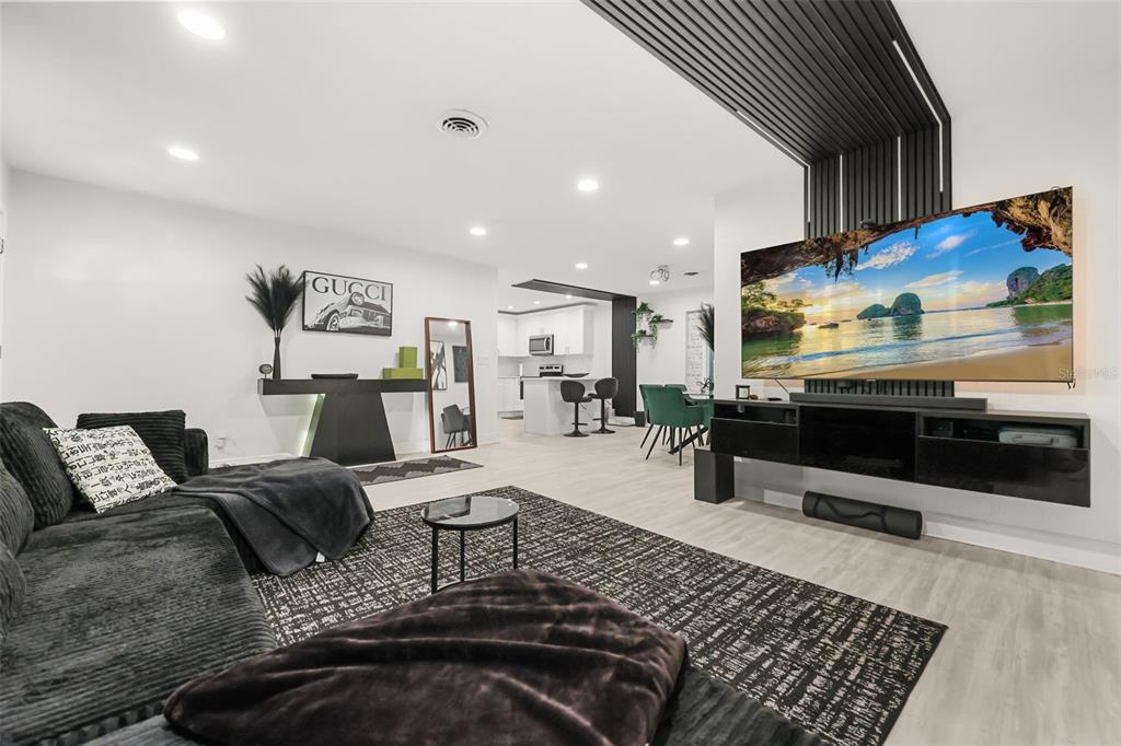 A modern living room features a large television, black furniture, and an open kitchen area — 2909 HARGILL DRIVE, ORLANDO, FL