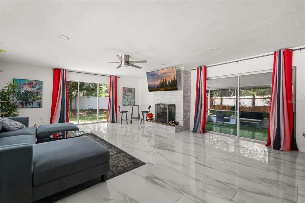 A living room features white marble-look tile floors, a fireplace with a mounted television, and sliding doors — 2909 HARGILL DRIVE, ORLANDO, FL