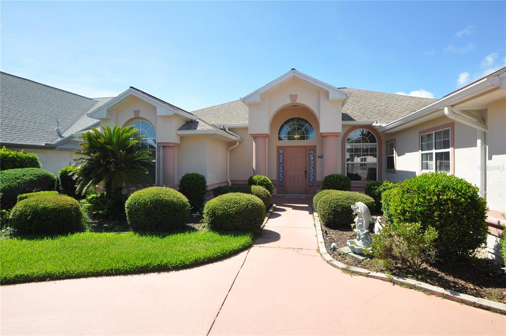 A single-story house with a beige stucco exterior, arched windows, and a paved walkway — 16 CEDARWOOD COURT, PALM COAST, FL