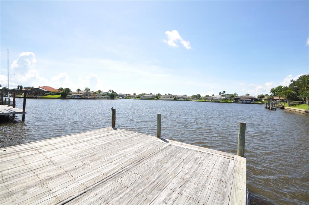 A wooden dock extends over a canal with residential homes visible in the background — 16 CEDARWOOD COURT, PALM COAST, FL