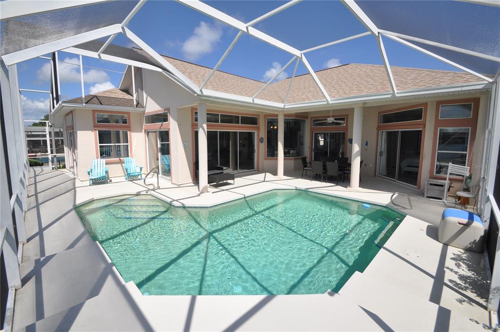 A swimming pool sits on a concrete patio enclosed by a screened lanai behind a house — 16 CEDARWOOD COURT, PALM COAST, FL