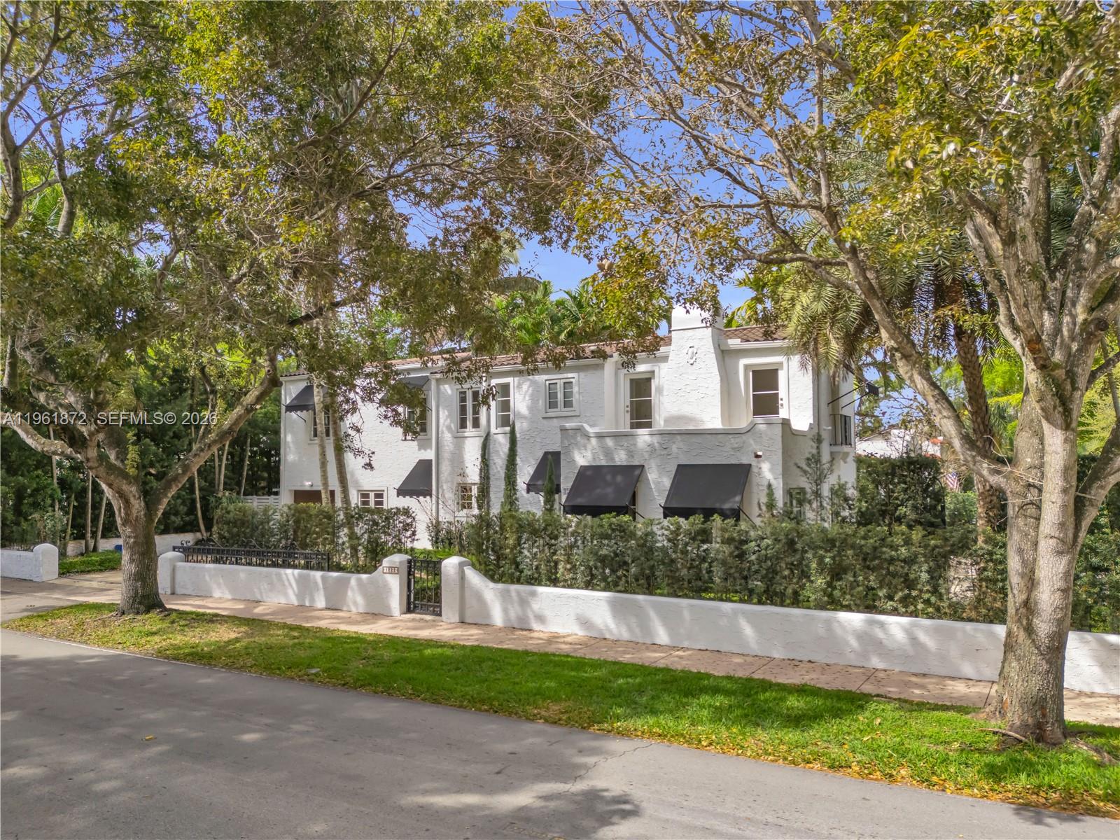 A two-story white stucco house features black awnings and a low perimeter wall — 1222 Cortez St, Coral Gables FL 33134, CORAL GABLES, FL