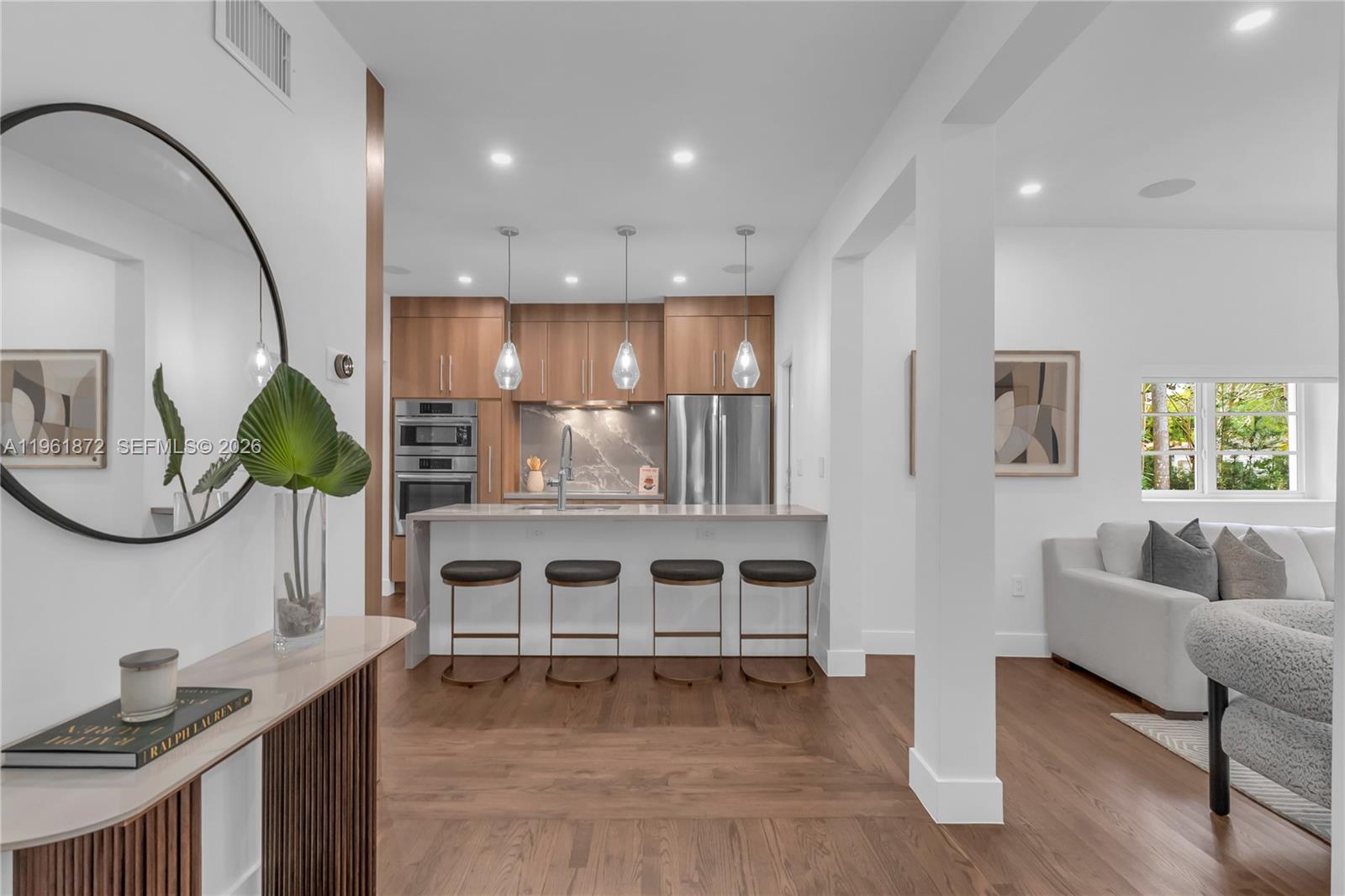 A modern kitchen features wood cabinets, a stone backsplash, and a breakfast bar with stools — 1222 Cortez St, Coral Gables FL 33134, CORAL GABLES, FL