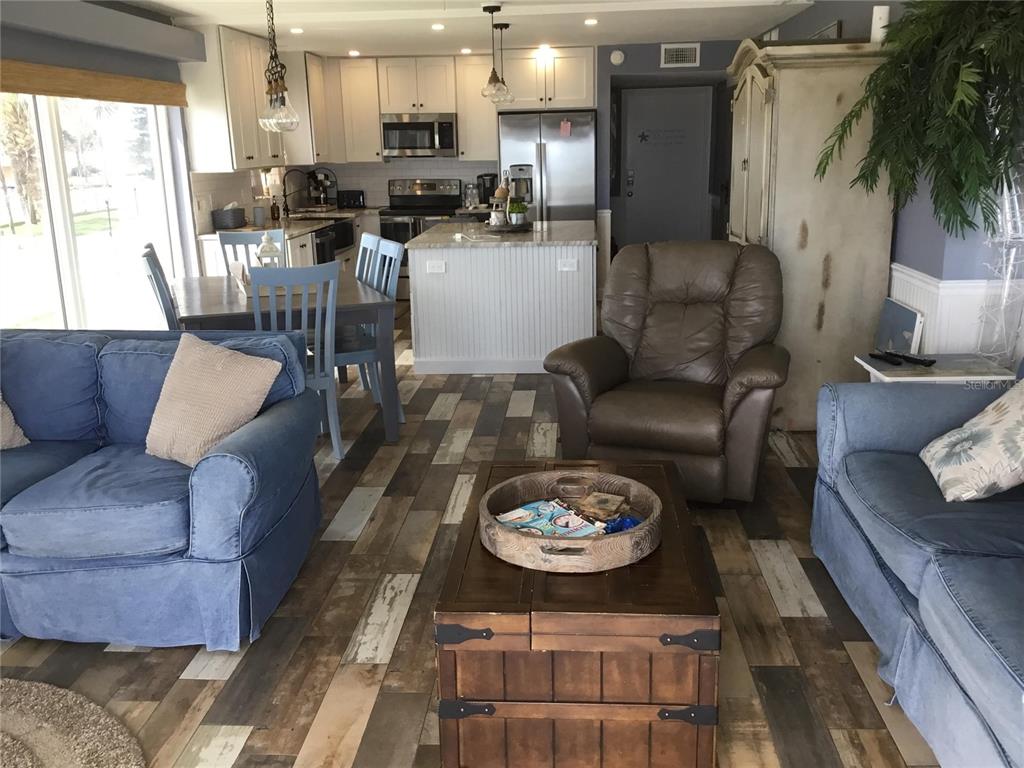 An open-concept living room and kitchen featuring wood-look flooring, blue sofas, and a central island — 1571 S ATLANTIC AVENUE UNIT 209, NEW SMYRNA BEACH, FL