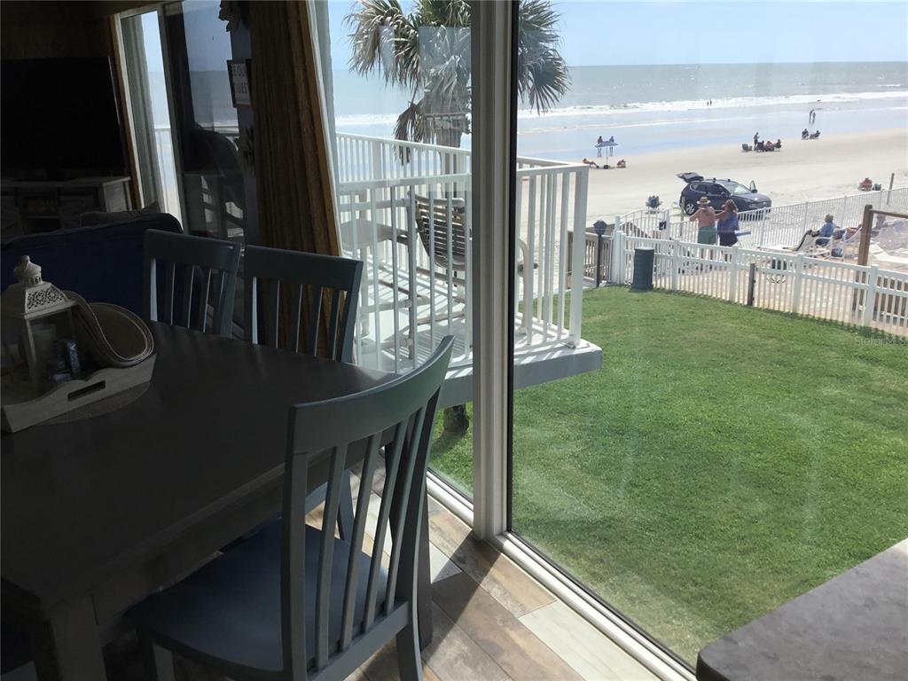 A dining area with gray chairs overlooks a grassy yard, a white fence, and the beach — 1571 S ATLANTIC AVENUE UNIT 209, NEW SMYRNA BEACH, FL