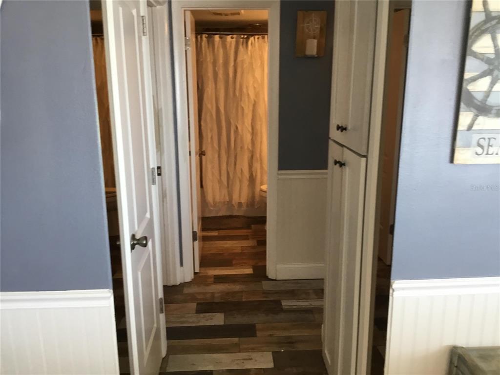 A hallway with wood-look flooring leads to a bathroom featuring a white shower curtain — 1571 S ATLANTIC AVENUE UNIT 209, NEW SMYRNA BEACH, FL