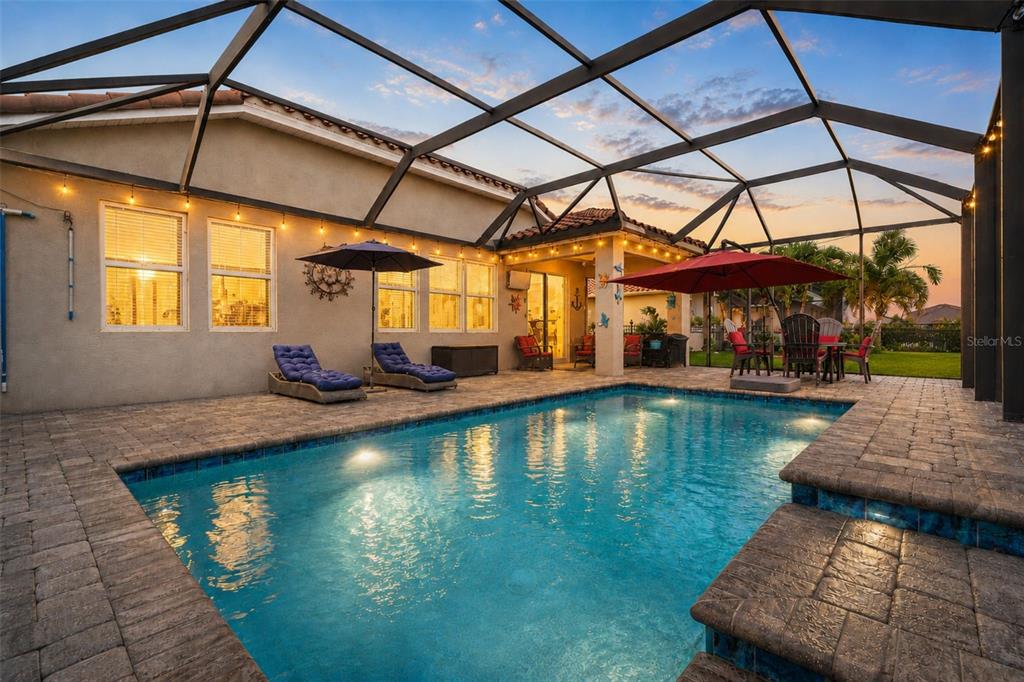 A swimming pool with a stone deck is enclosed by a screened lanai at sunset — 13212 SAW PALM CREEK TRAIL, LAKEWOOD RANCH, FL