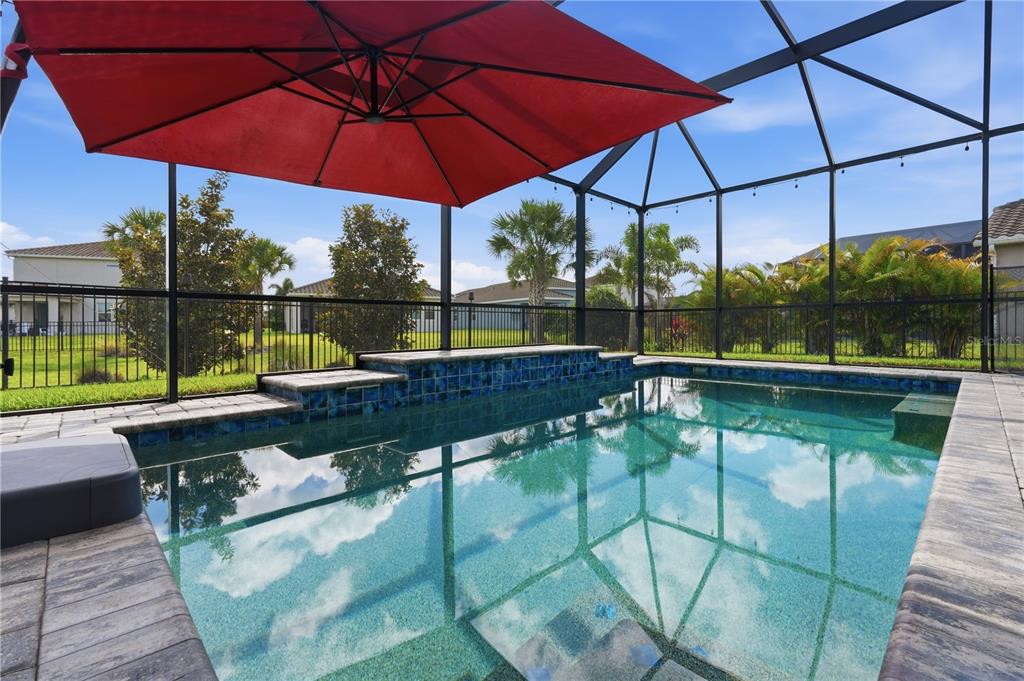 A screened-in swimming pool with a red umbrella and a tiled water feature — 13212 SAW PALM CREEK TRAIL, LAKEWOOD RANCH, FL