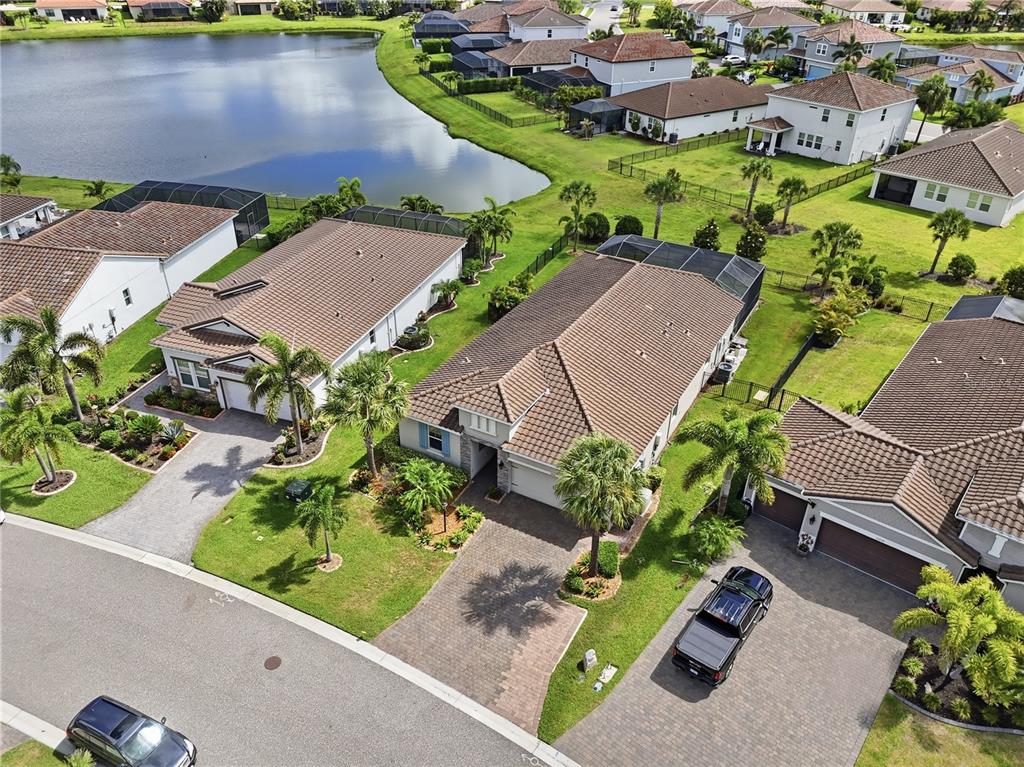 An aerial view shows several suburban houses with tiled roofs, driveways, and a nearby lake — 13212 SAW PALM CREEK TRAIL, LAKEWOOD RANCH, FL