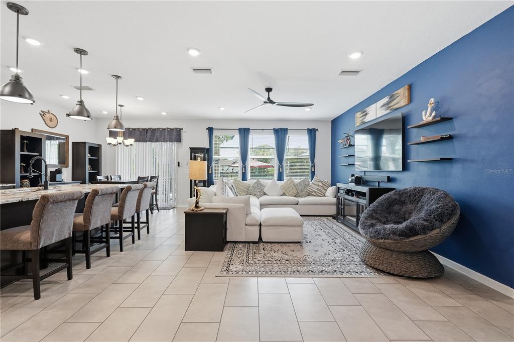 An open-concept living room features a blue accent wall, a sectional sofa, and kitchen seating — 13212 SAW PALM CREEK TRAIL, LAKEWOOD RANCH, FL