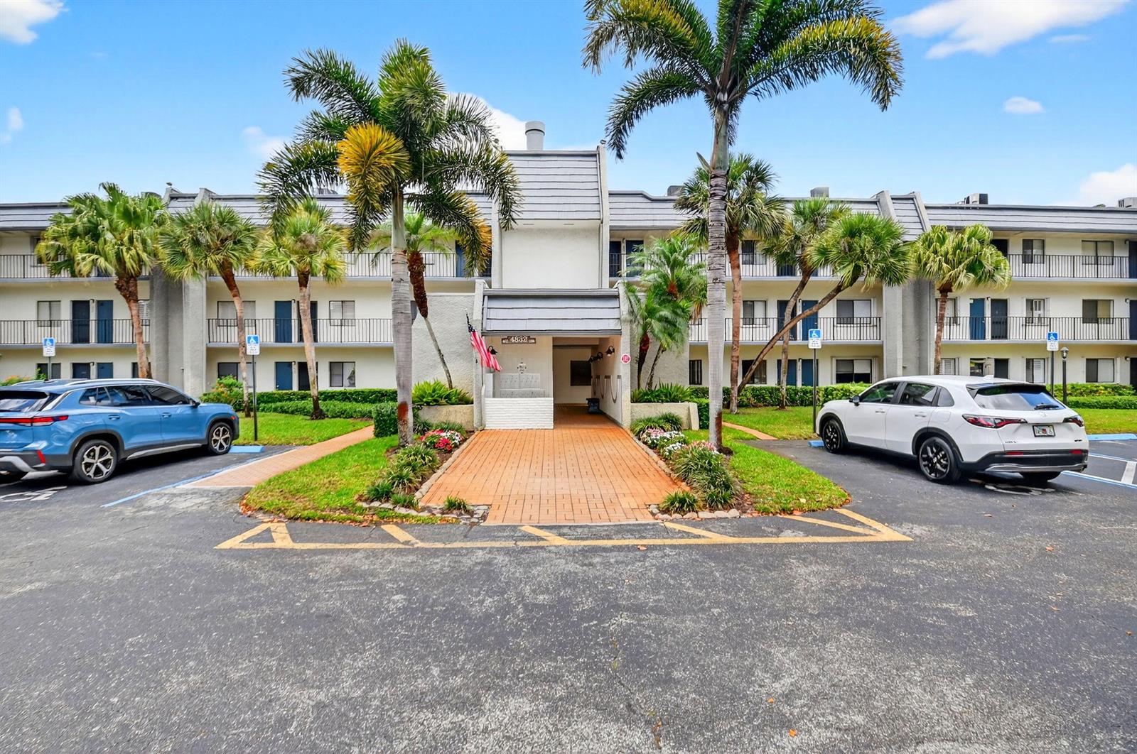 A multi-story apartment building exterior features a brick walkway, palm trees, and parking spaces — 4832 Esedra Court # 103, FL 33467, FL