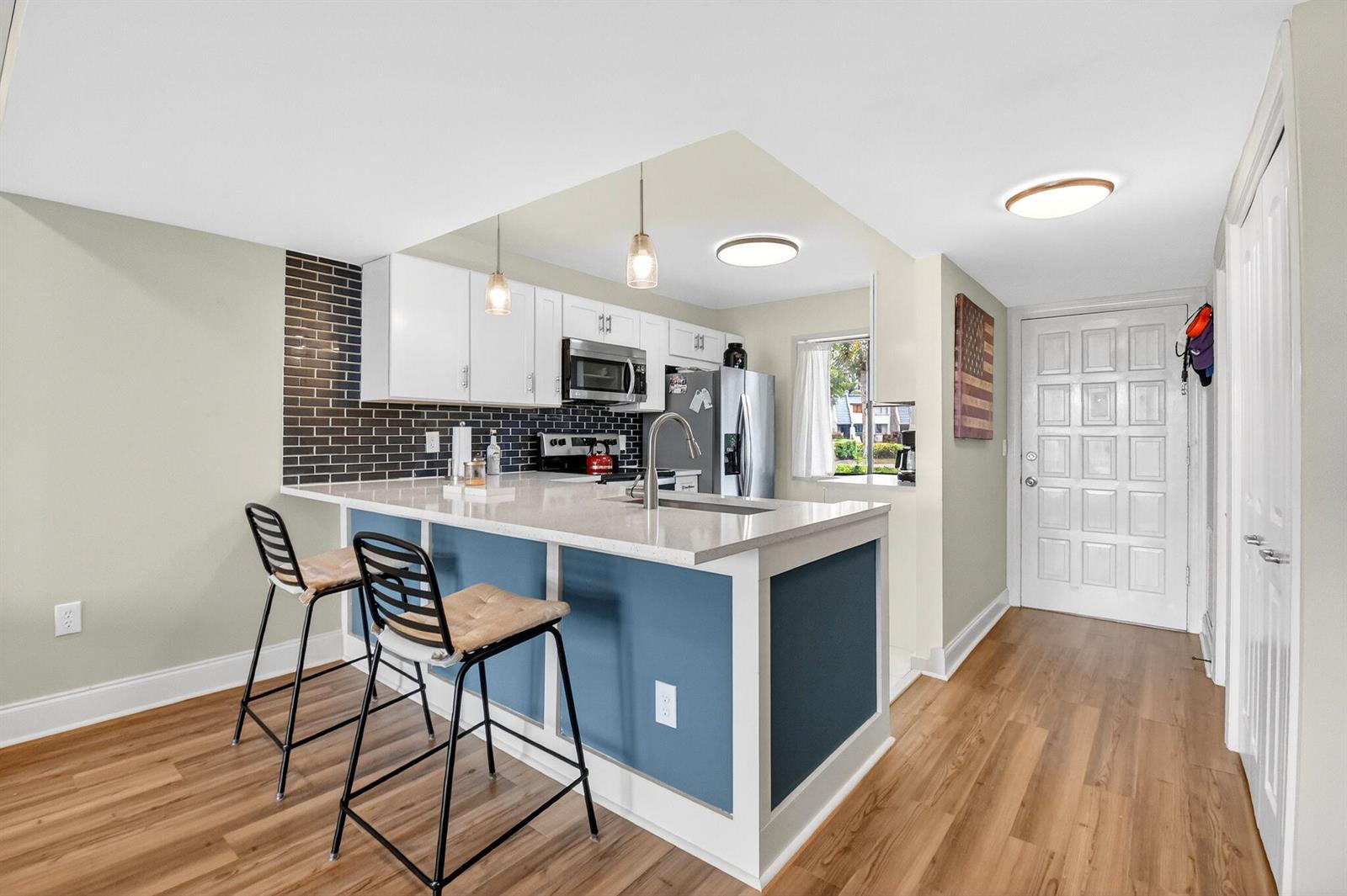 A kitchen features a blue island with a sink, white cabinets, and dark tile backsplash — 4832 Esedra Court # 103, FL 33467, FL