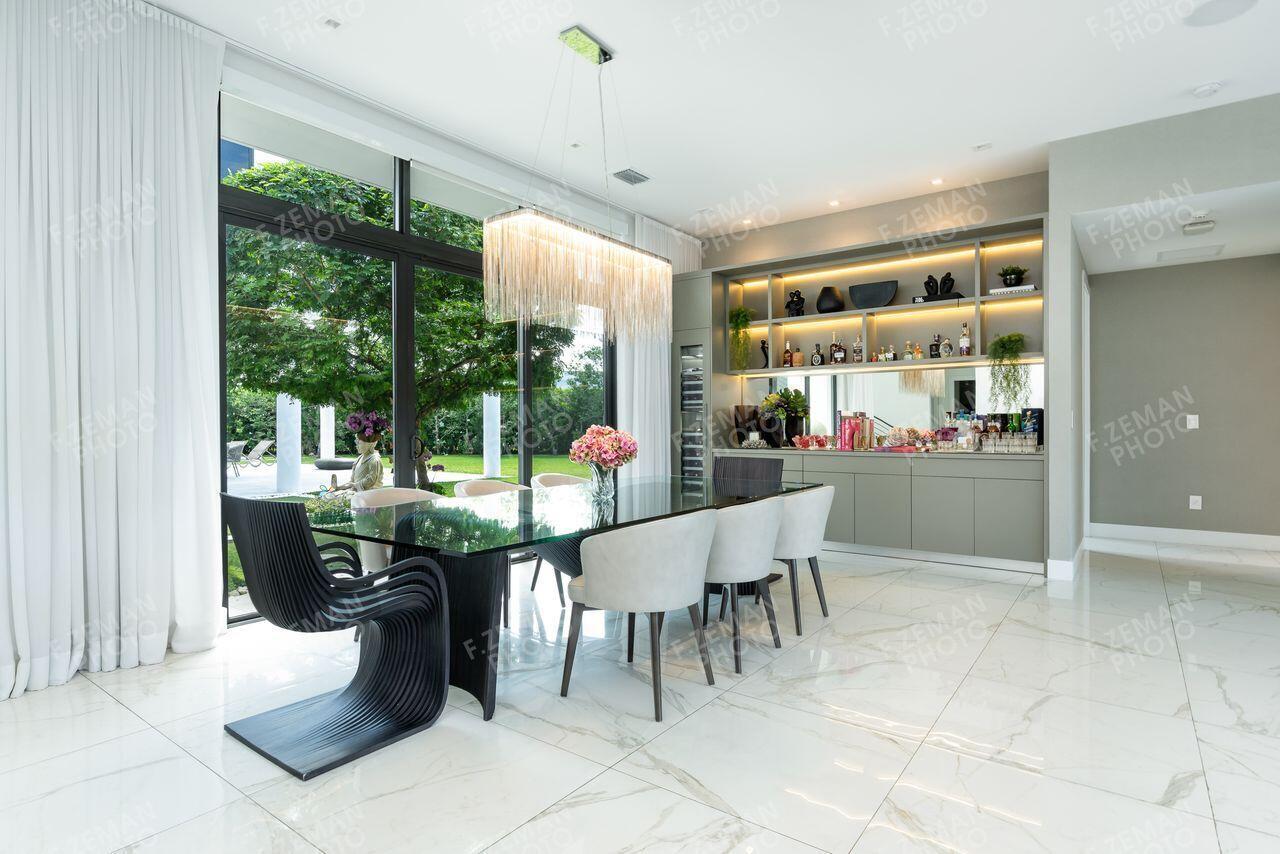 A modern dining room features a glass table, sculptural chairs, and a built-in bar area — 16550 Sunset Way, Weston FL 33326, WESTON, FL