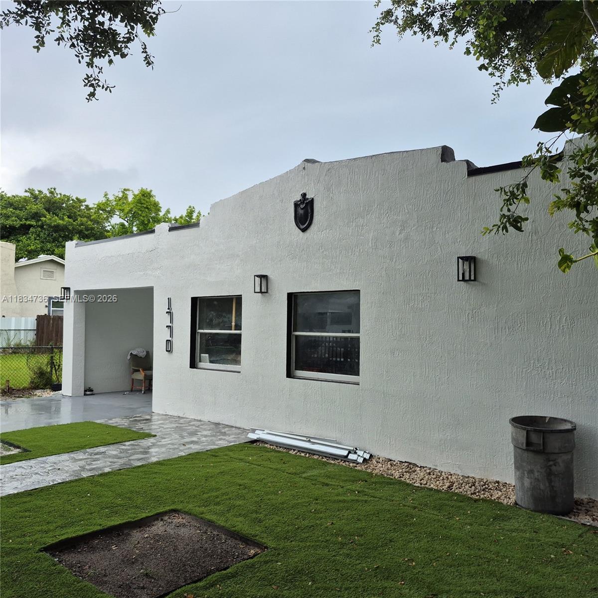 A white stucco house exterior features a covered entryway, two windows, and artificial turf landscaping — 1770 NW 44th St, Miami FL 33142, MIAMI, FL