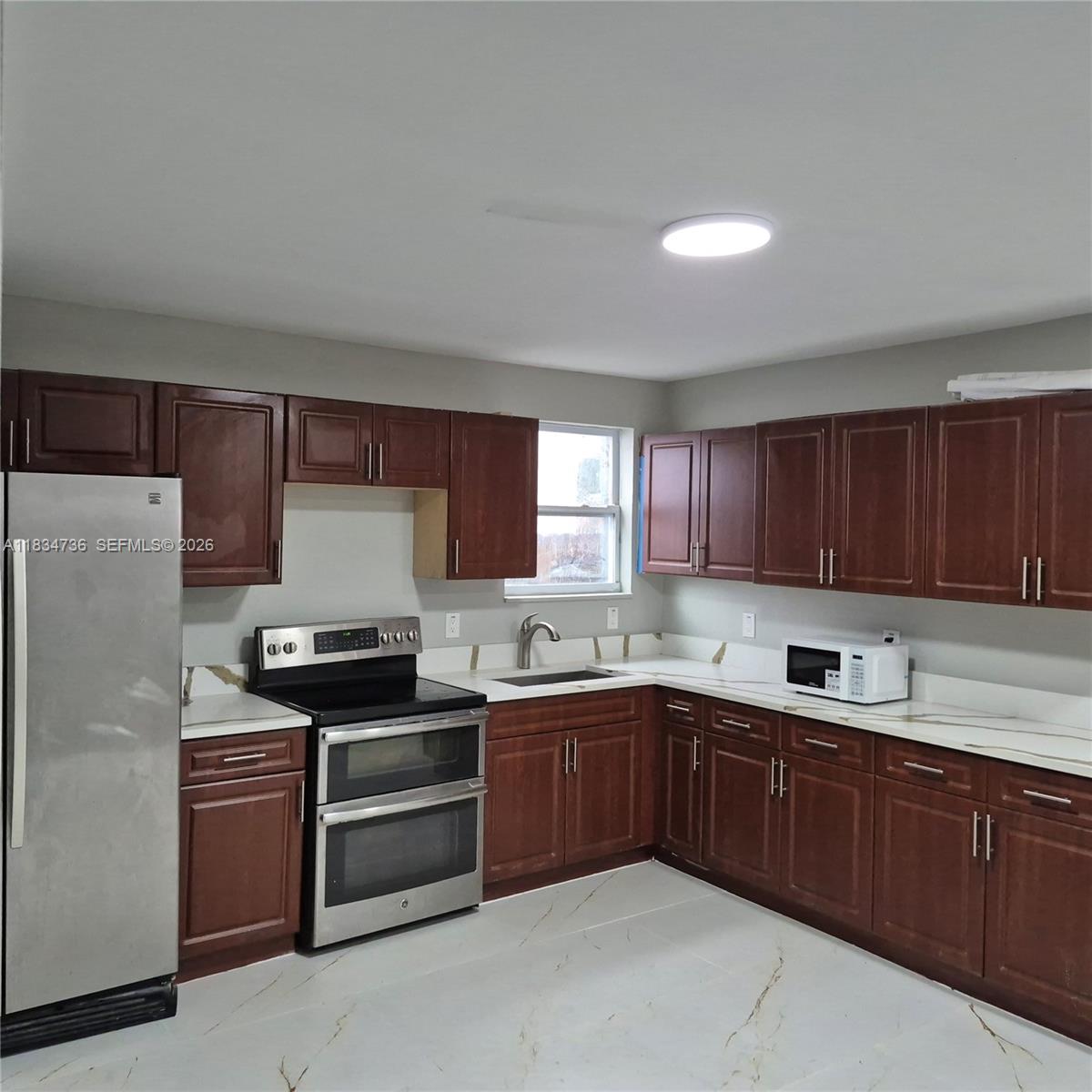 A kitchen features dark wood cabinets, stainless steel appliances, and white countertops with gold veining — 1770 NW 44th St, Miami FL 33142, MIAMI, FL