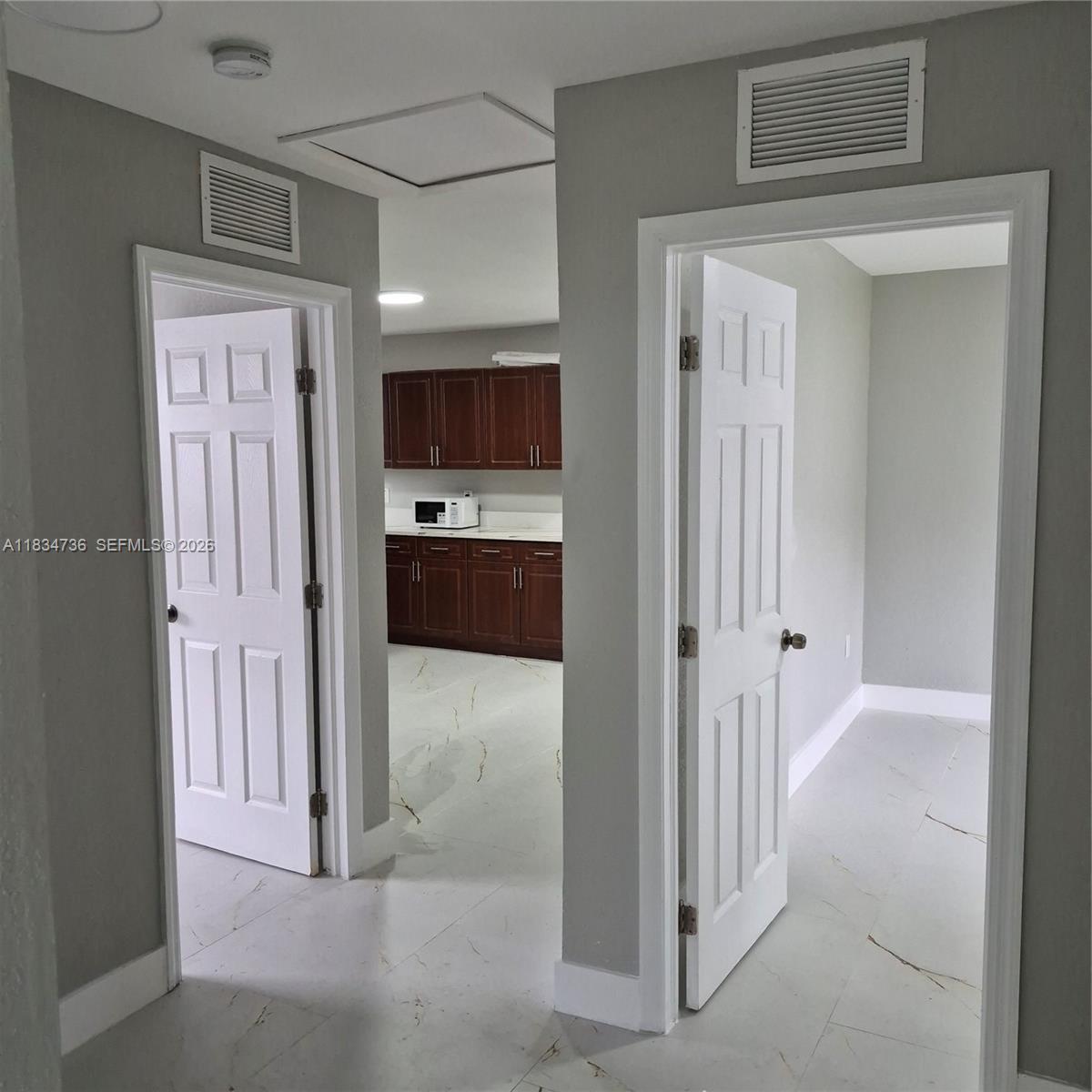 A hallway with white doors leads to a kitchen featuring dark wood cabinets — 1770 NW 44th St, Miami FL 33142, MIAMI, FL