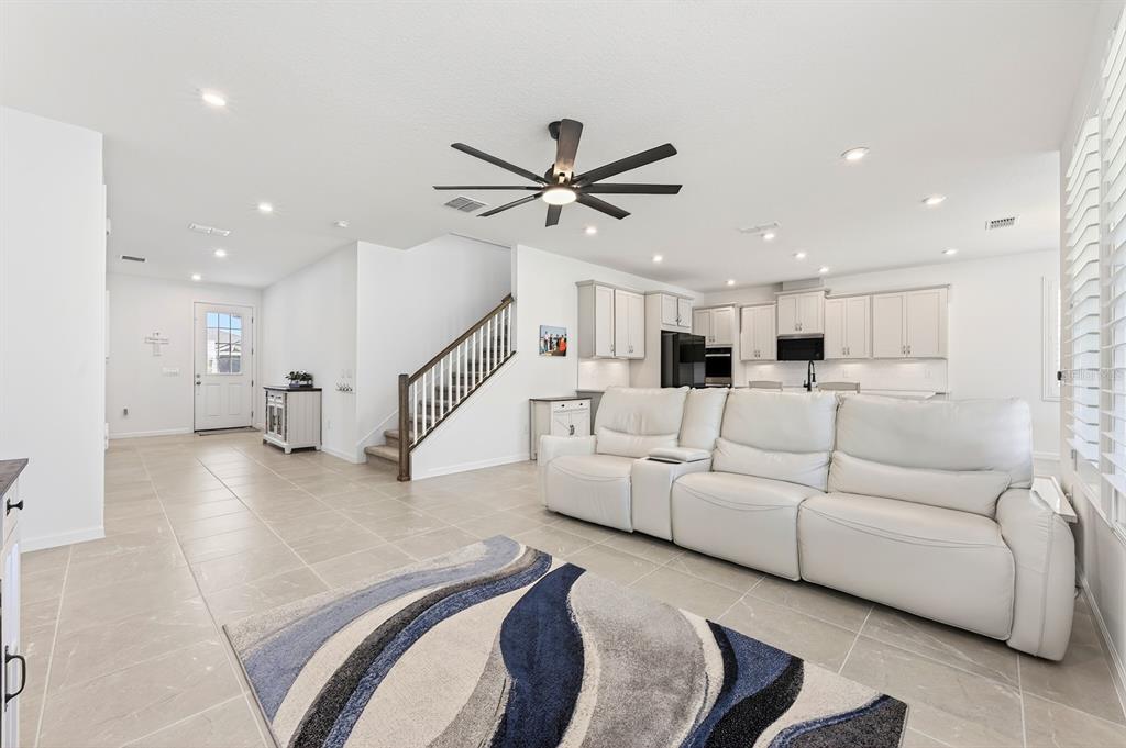 A bright, open-concept living room features light tile flooring, a white sectional, and a staircase — 3520 BANANA SHRUB BOULEVARD, CLERMONT, FL