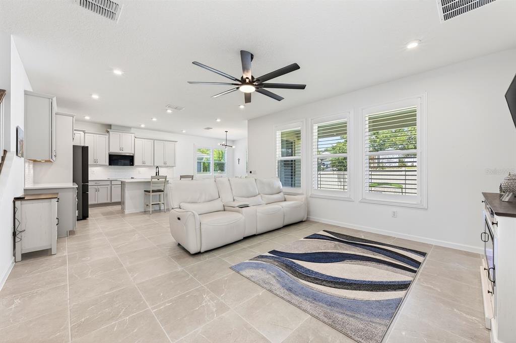 A bright open-concept living room features light tile floors, a white sofa, and a kitchen — 3520 BANANA SHRUB BOULEVARD, CLERMONT, FL
