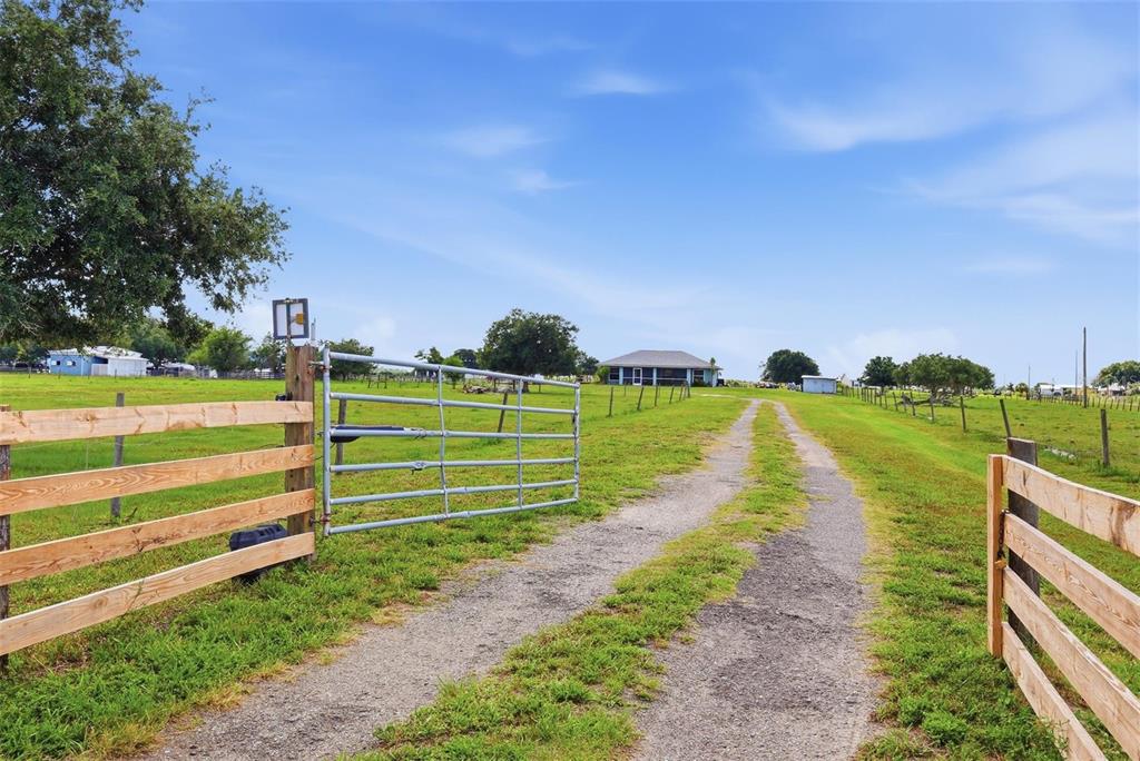 A gravel driveway leads through a metal gate toward a house on a grassy lot — 13105 MJ ROAD, MYAKKA CITY, FL