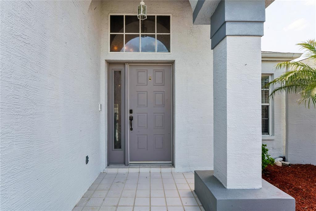 The exterior entryway features a gray front door, a sidelight, and a tiled porch — 1018 CASTILLE DRIVE, SPRING HILL, FL