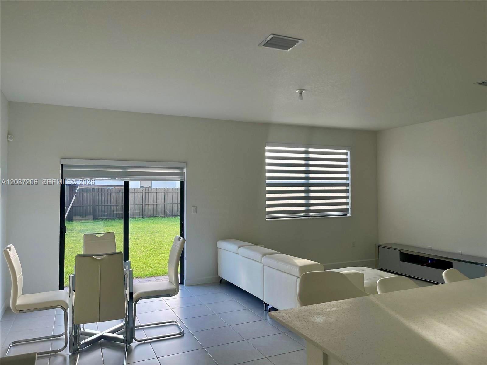 A bright living and dining area features white tile floors, a white sofa, and sliding doors — 22960 SW 130th Ave, Miami FL 33170, MIAMI, FL