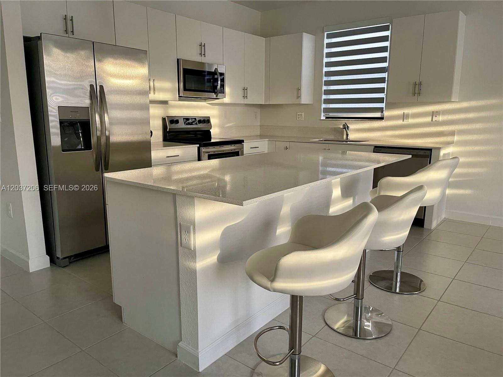 A modern kitchen features white cabinets, stainless steel appliances, a quartz island, and bar stools — 22960 SW 130th Ave, Miami FL 33170, MIAMI, FL