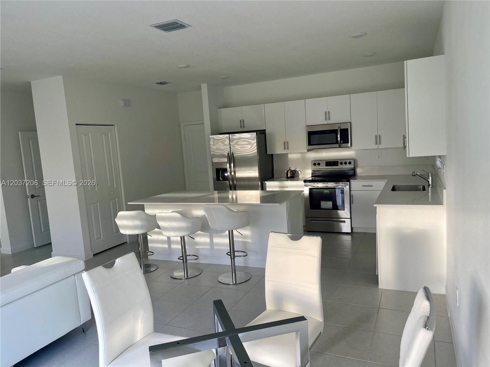 A modern kitchen features white cabinetry, stainless steel appliances, and a central island with stools — 22960 SW 130th Ave, Miami FL 33170, MIAMI, FL