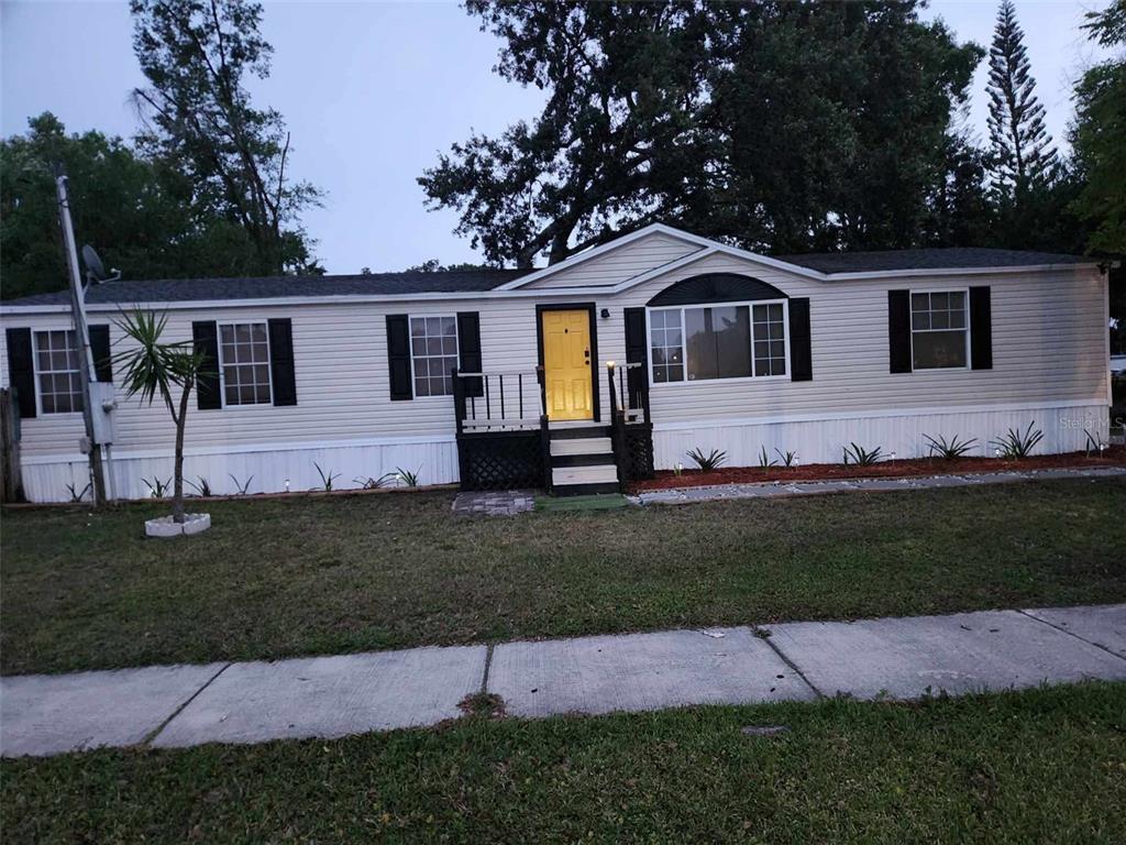 A single-story manufactured home with light siding, a yellow front door, and a small porch — 9653 4TH AVENUE, ORLANDO, FL