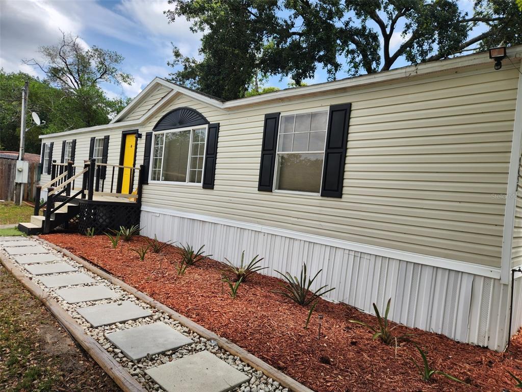 A single-story manufactured home with beige siding, black shutters, and a yellow front door — 9653 4TH AVENUE, ORLANDO, FL
