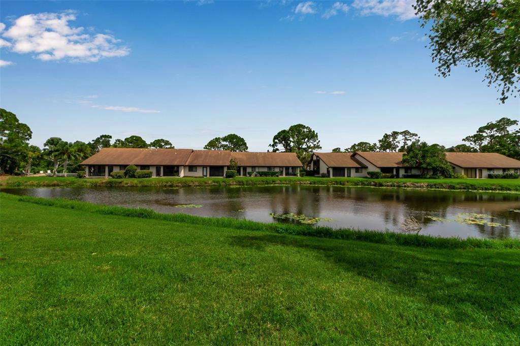 A view of a pond in front of a row of single-story residential buildings — 5224 LAKE VILLAGE DRIVE UNIT 67, SARASOTA, FL