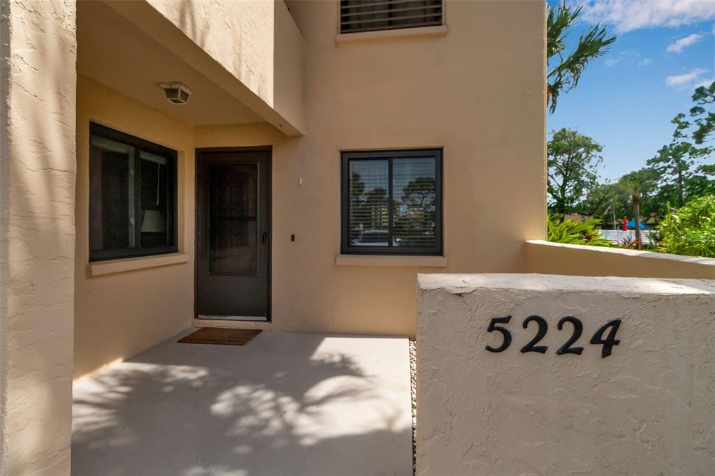 The exterior view shows a tan stucco building entrance with a front door and windows — 5224 LAKE VILLAGE DRIVE UNIT 67, SARASOTA, FL