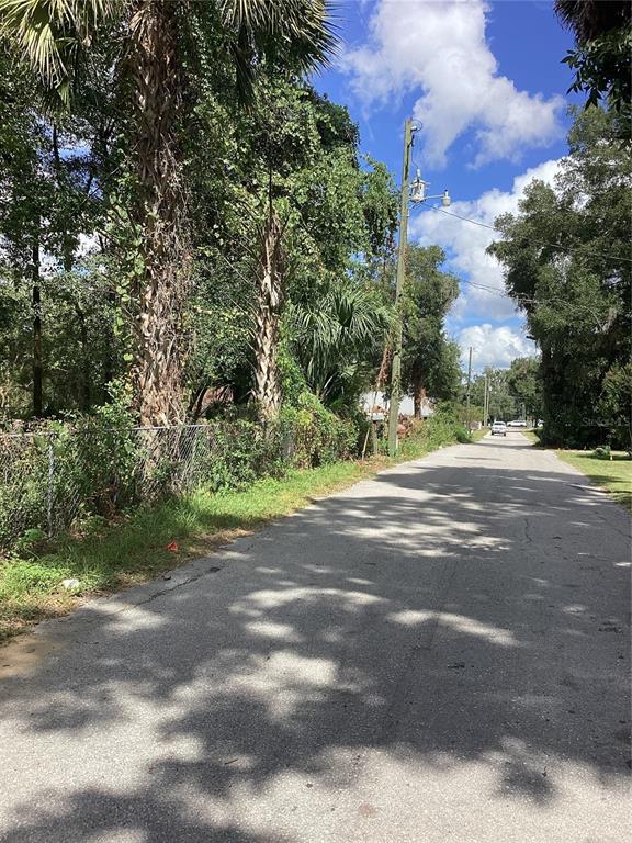 A paved road runs alongside a chain-link fence and tall trees under a blue sky — 0 NW 9TH STREET, OCALA, FL