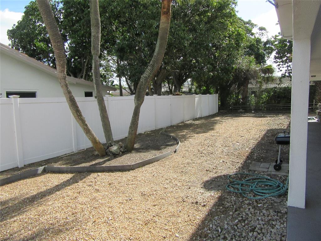 A backyard features a gravel ground, a white vinyl fence, and a large tree — 110 60TH AVENUE UNIT 1, ST PETE BEACH, FL