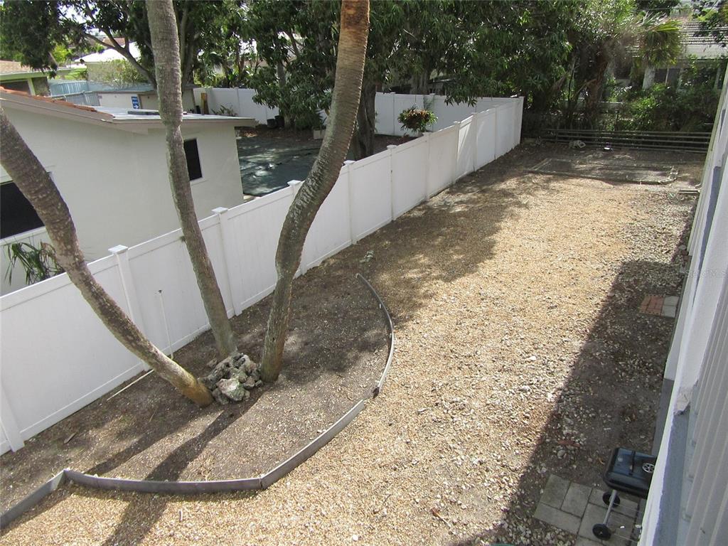 A backyard features a gravel ground area, a white vinyl fence, and two large trees — 110 60TH AVENUE UNIT 1, ST PETE BEACH, FL