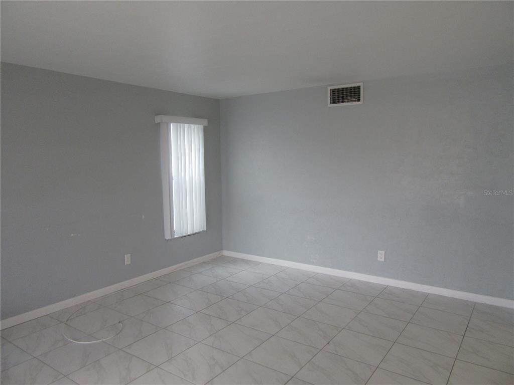 An empty room features light gray walls, white baseboards, and light-colored tile flooring — 110 60TH AVENUE UNIT 1, ST PETE BEACH, FL