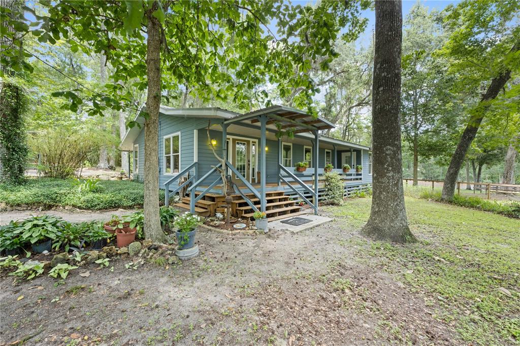 A blue house with a wooden porch and stairs sits in a wooded yard — 18251 NW 141ST AVENUE, WILLISTON, FL
