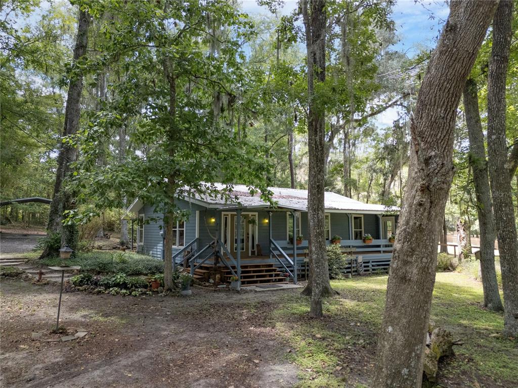 A blue house with a metal roof and a wooden porch sits among many trees — 18251 NW 141ST AVENUE, WILLISTON, FL