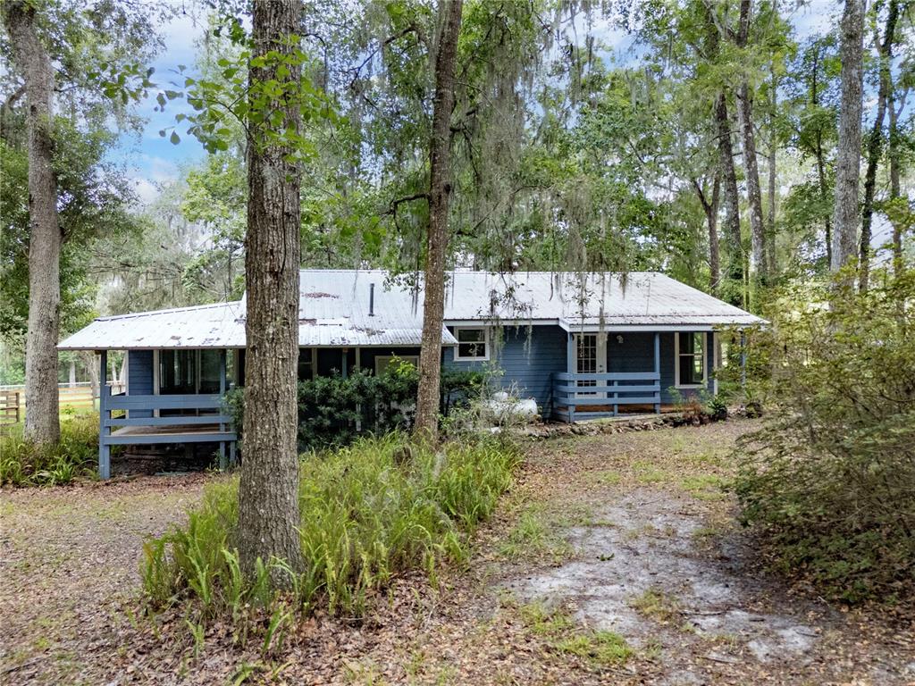 A blue house with a metal roof sits in a wooded area with a porch — 18251 NW 141ST AVENUE, WILLISTON, FL