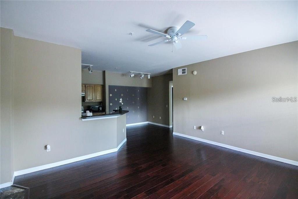 An open-concept living area features dark hardwood floors, a ceiling fan, and a kitchen pass-through — 6029 WESTGATE DRIVE UNIT 725, ORLANDO, FL