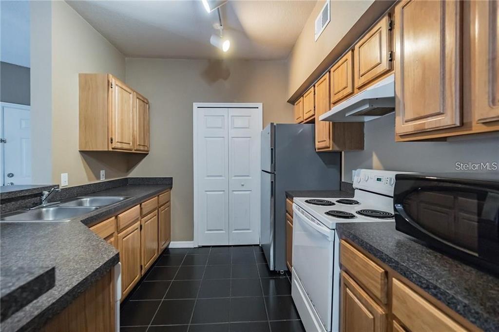 A kitchen features wood cabinets, dark countertops, white appliances, and black tile flooring — 6029 WESTGATE DRIVE UNIT 725, ORLANDO, FL