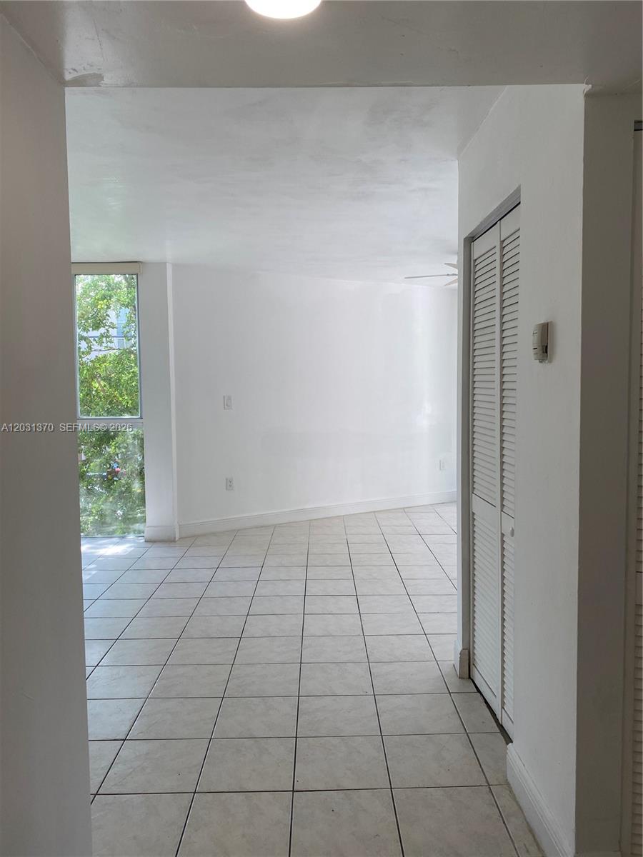 A bright, empty room features white walls, tiled flooring, and a large window with greenery — 7075 NW 186th St # C308, Hialeah FL 33015, HIALEAH, FL