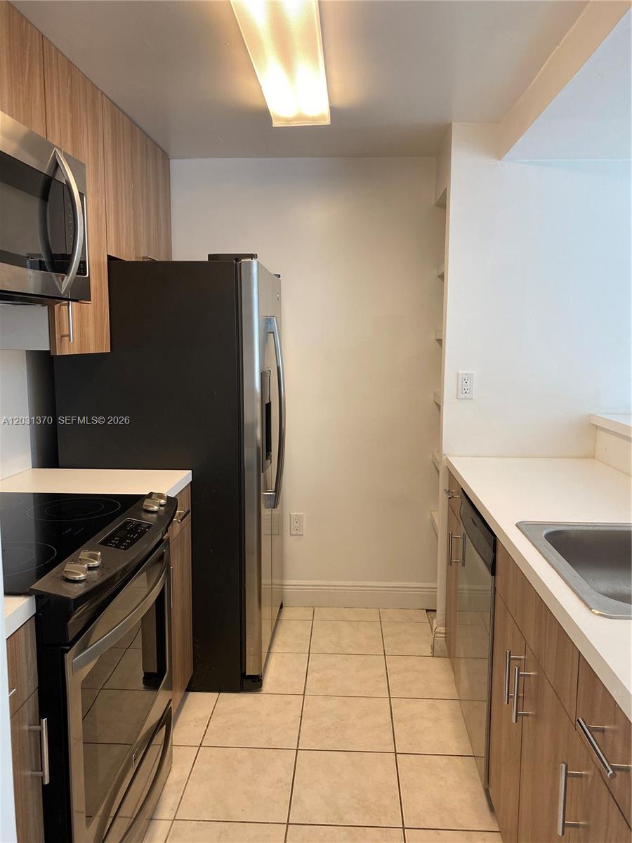 A galley kitchen features stainless steel appliances, light wood cabinets, and white countertops — 7075 NW 186th St # C308, Hialeah FL 33015, HIALEAH, FL