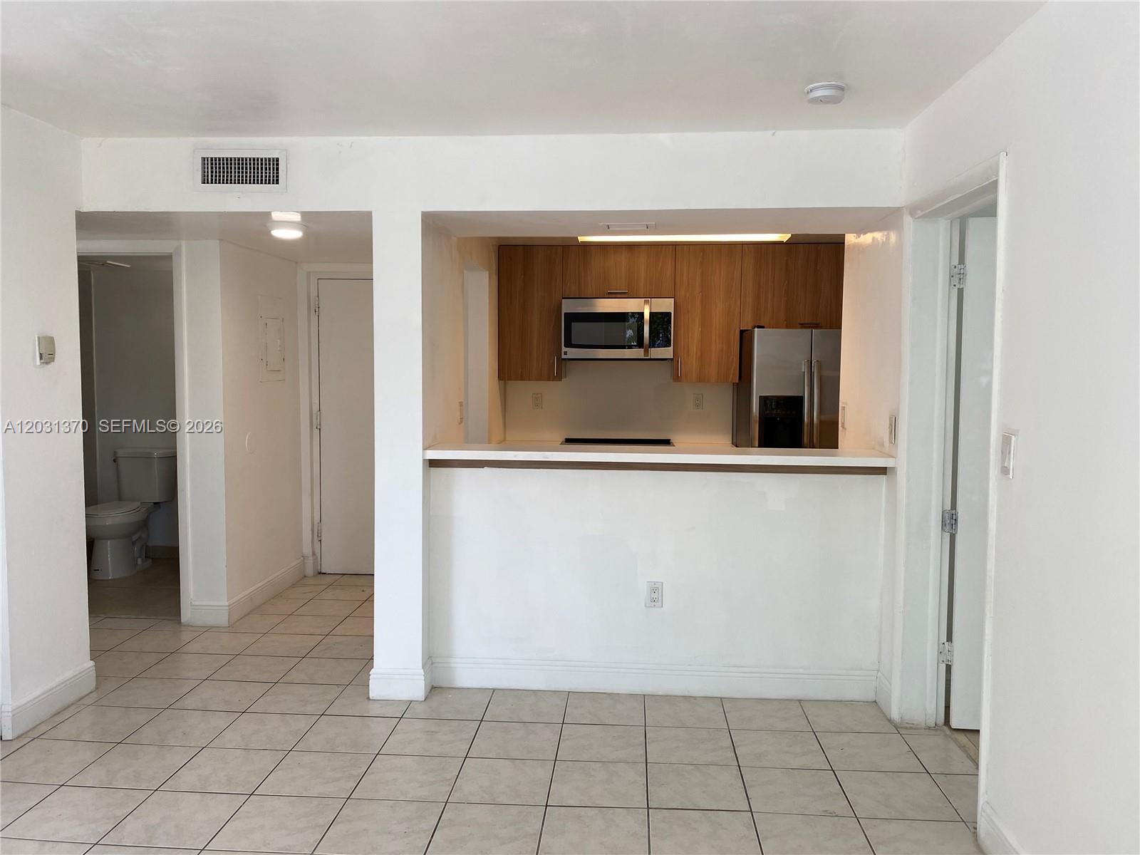 A kitchen with wood cabinets and stainless steel appliances overlooks a tiled living area — 7075 NW 186th St # C308, Hialeah FL 33015, HIALEAH, FL