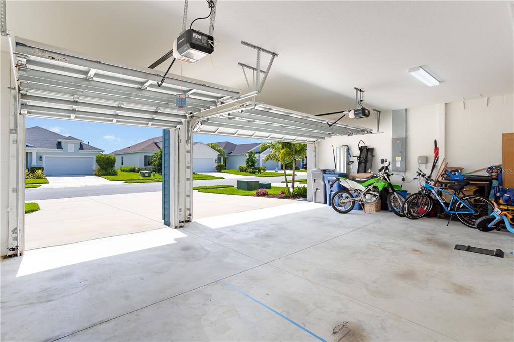 An open two-car garage with concrete floors, a dirt bike, and bicycles parked inside — 3410 BOX TURTLE TERRACE, PARRISH, FL