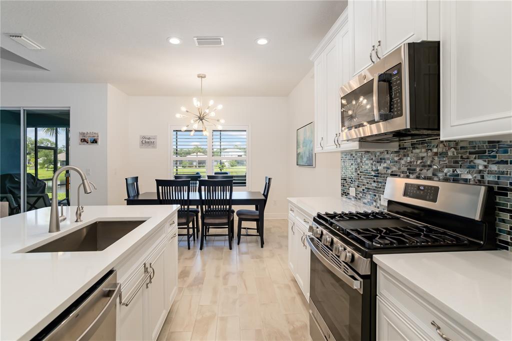 A modern kitchen with white cabinets, stainless steel appliances, and an island overlooks a dining area — 3410 BOX TURTLE TERRACE, PARRISH, FL