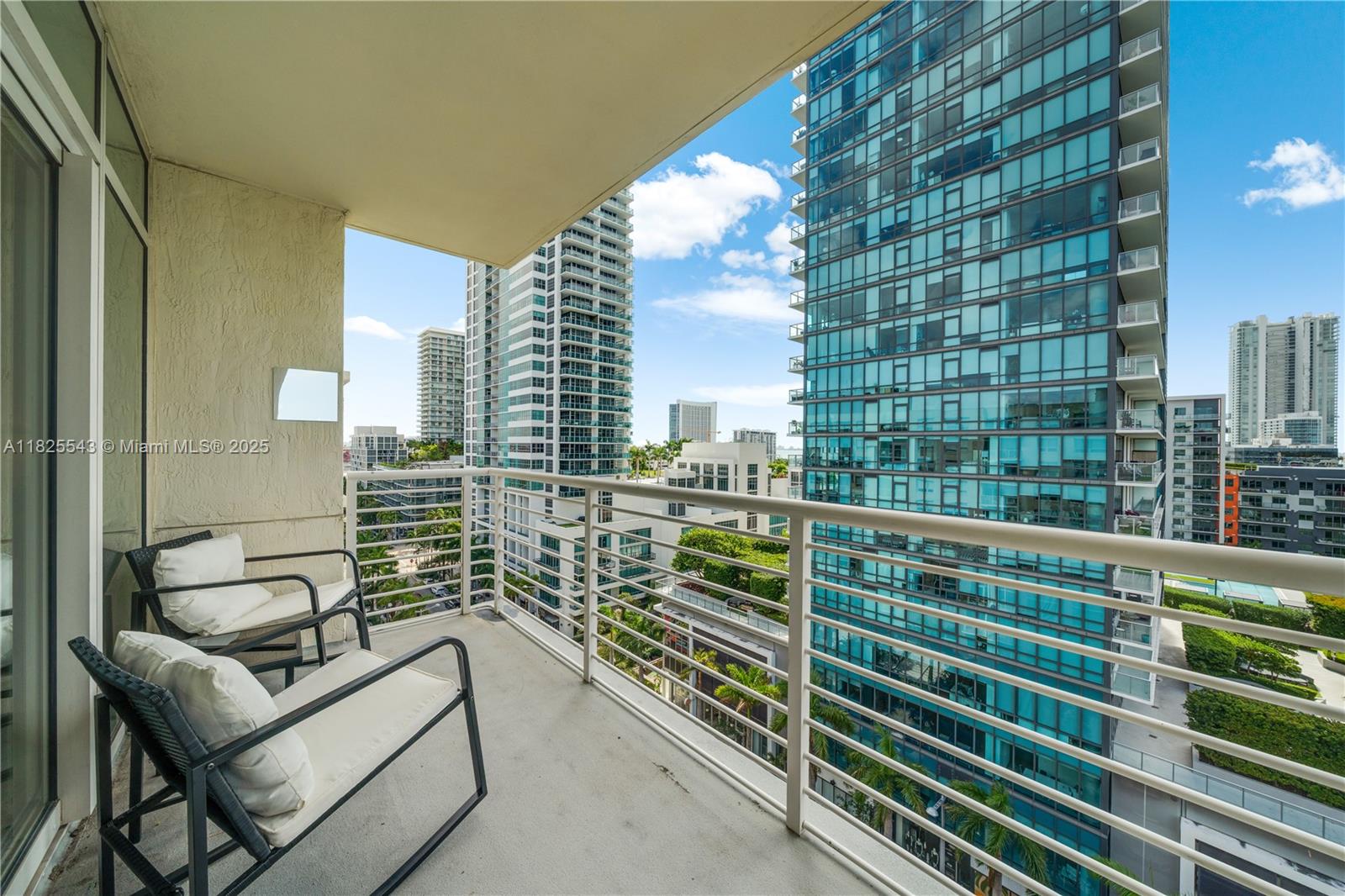 A balcony with two chairs overlooks a city skyline featuring several modern high-rise buildings — 3250 NE 1st Ave # 1016, Miami FL 33137, MIAMI, FL