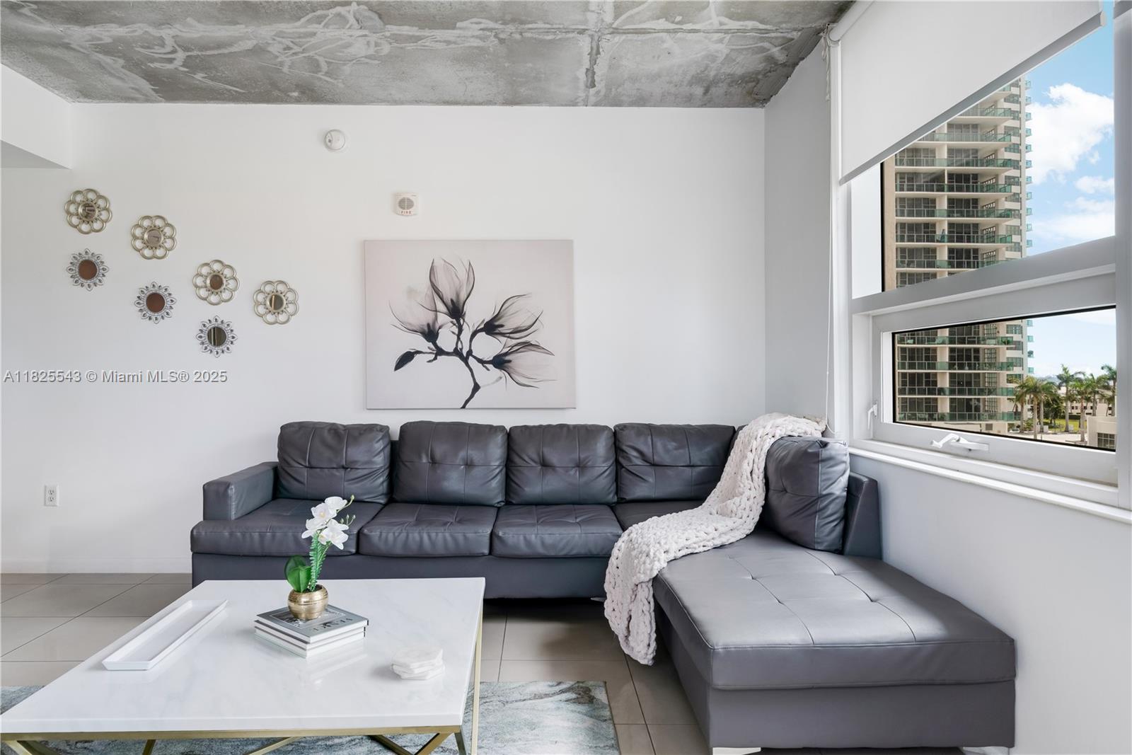 A living room features a gray sectional sofa, a white coffee table, and exposed concrete ceilings — 3250 NE 1st Ave # 1016, Miami FL 33137, MIAMI, FL